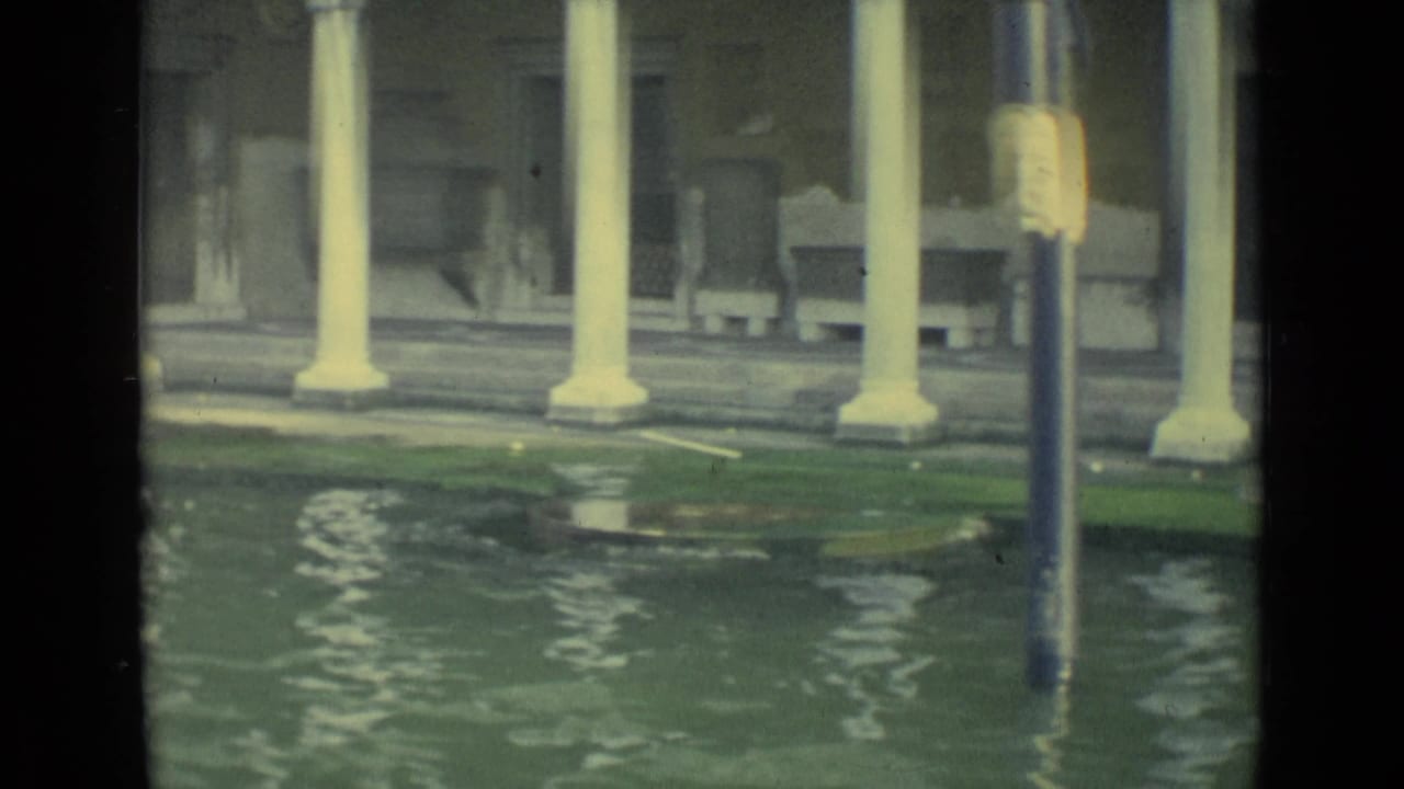 1962 Venice canal-side view with high water, white columns, a dark doorway, benches, and a lamppost rising from the floodwater.