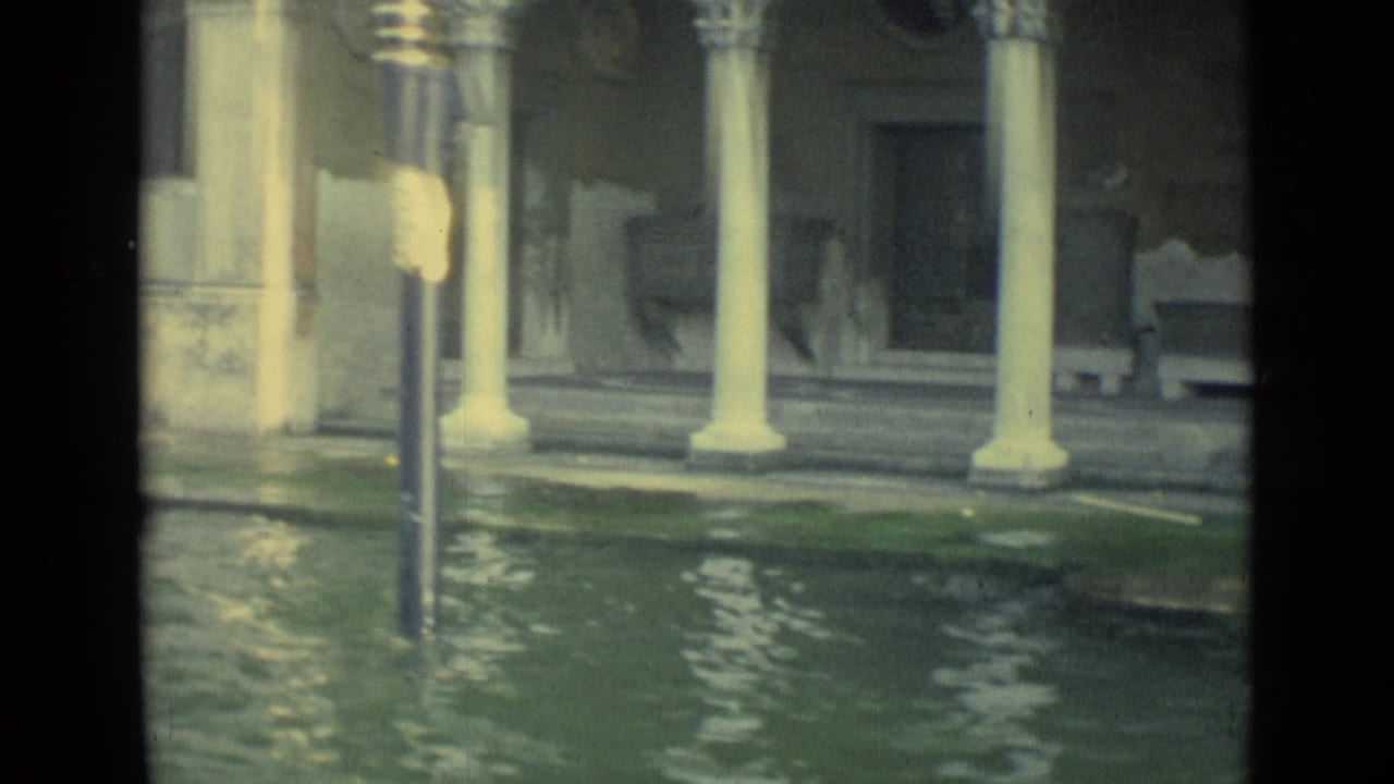 1962 Venice 8mm view of floodwater, pale columns, weathered masonry, a lamppost, and a small boat near the canal edge.