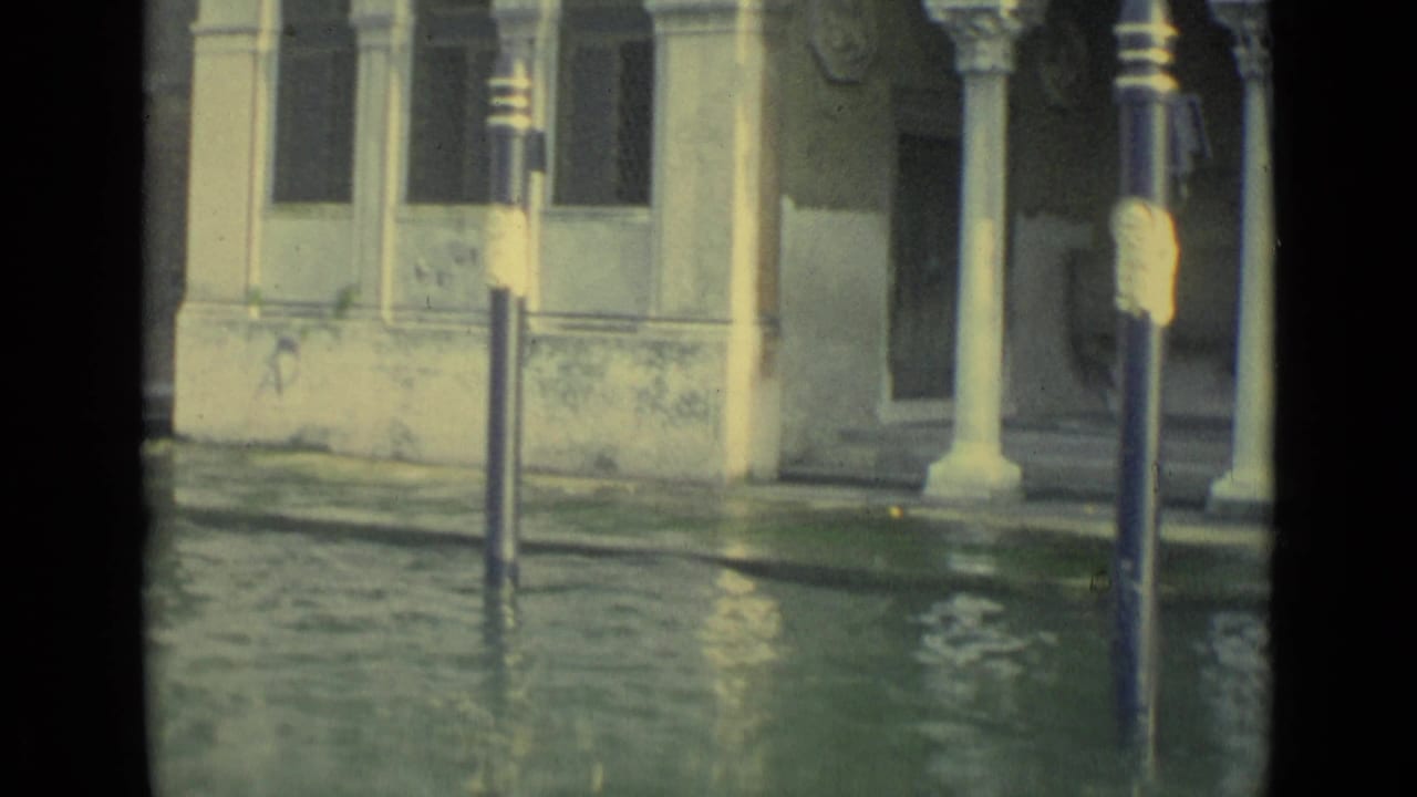 1962 Venice frame with green floodwater, a lamppost, pale columns, and weathered building details along the canal.