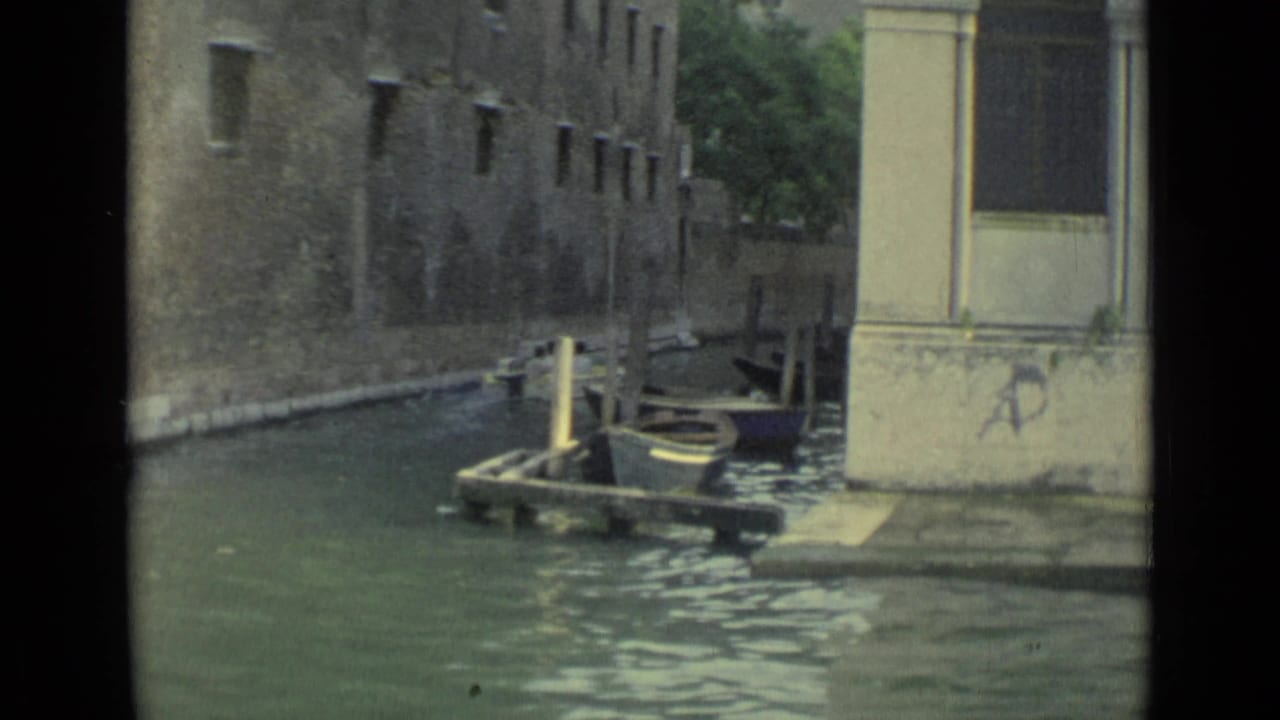 Narrow Venice canal with empty boats moored beside weathered stone buildings.