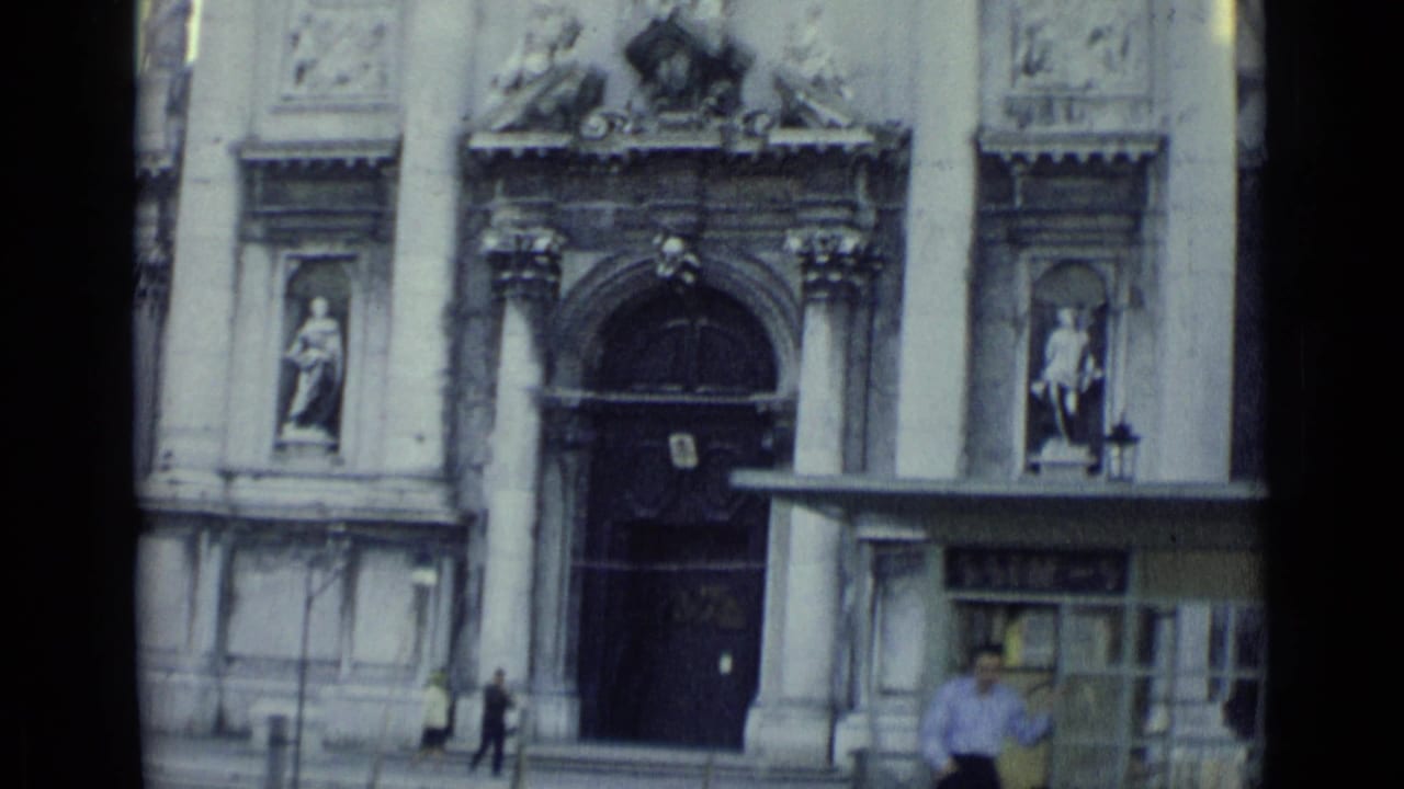 1962 Venice church entrance with statues, columns, a kiosk or shelter, and a few distant pedestrians near the doorway.