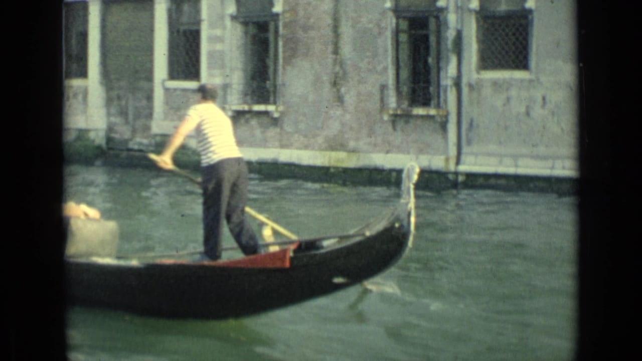 Gondolier standing at the stern of a gondola in a narrow canal.