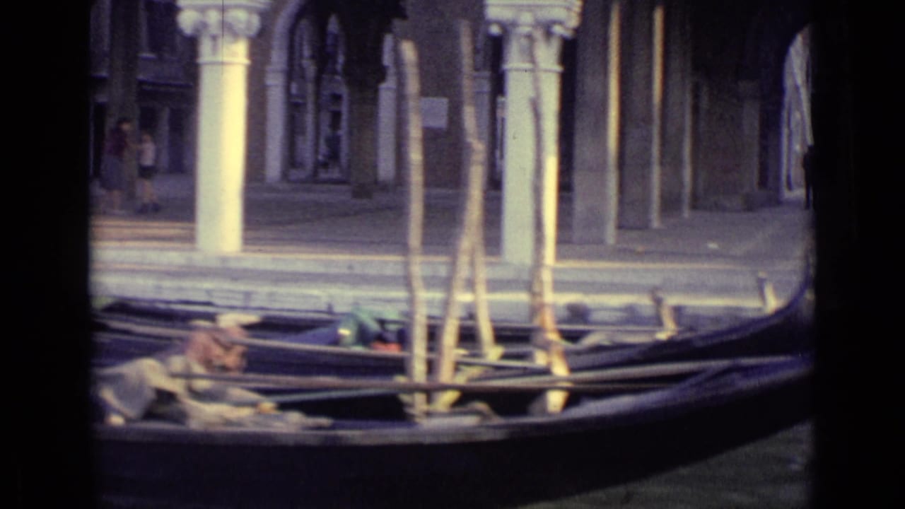 Gondolas moored on a Venice canal beside stone columns and arcaded buildings.