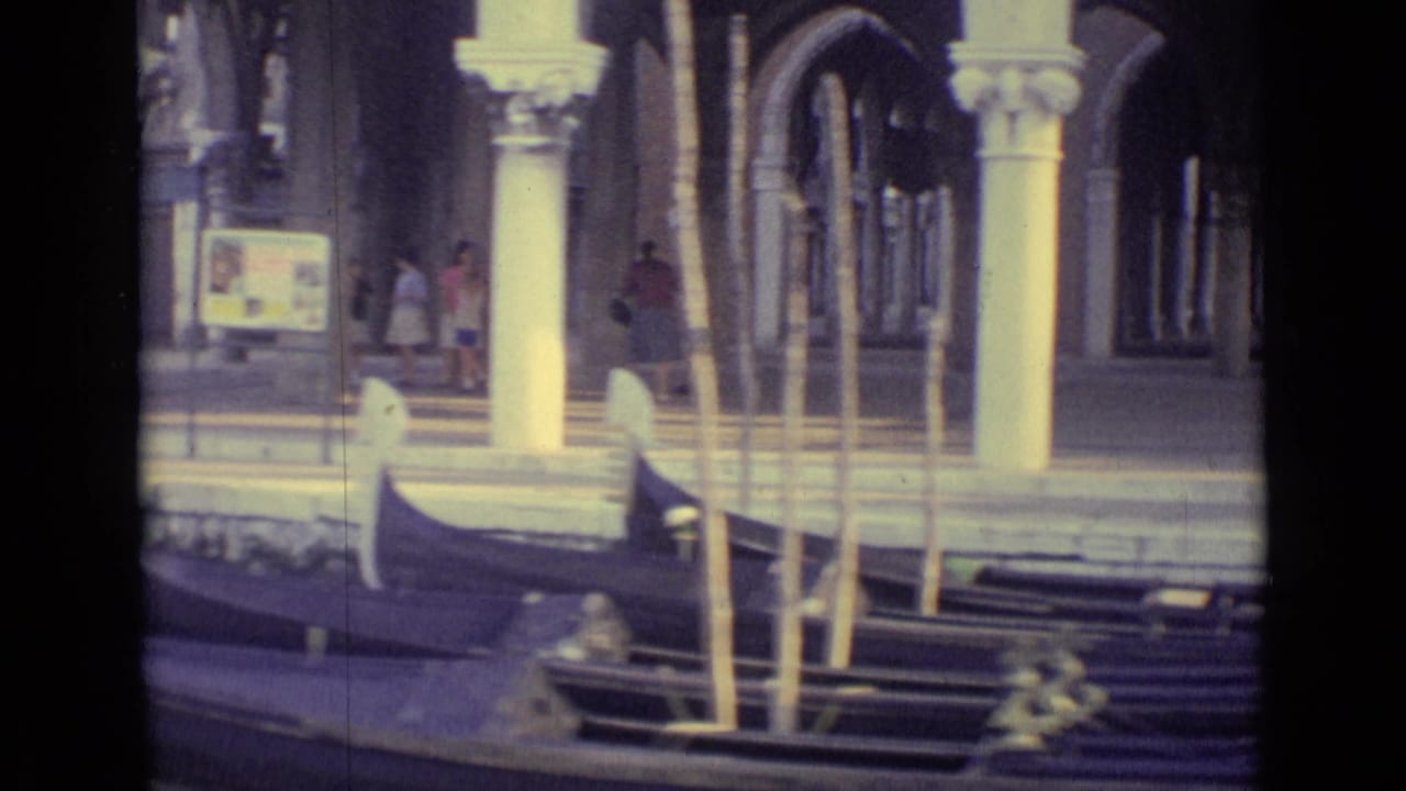 Venice canal scene from 1962 home-movie footage, showing a gondola near the water edge and pedestrians under columned arcades.