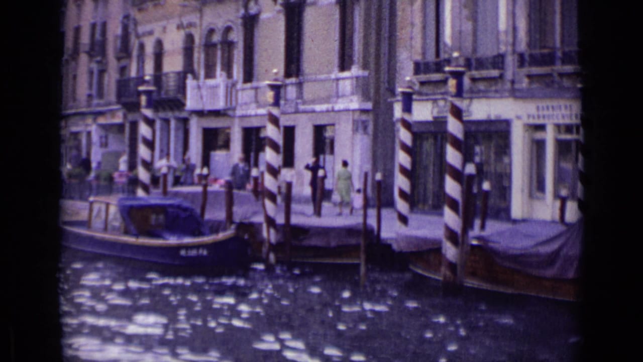 Small motorboat on a Venice canal beside striped mooring posts and historic building fronts.