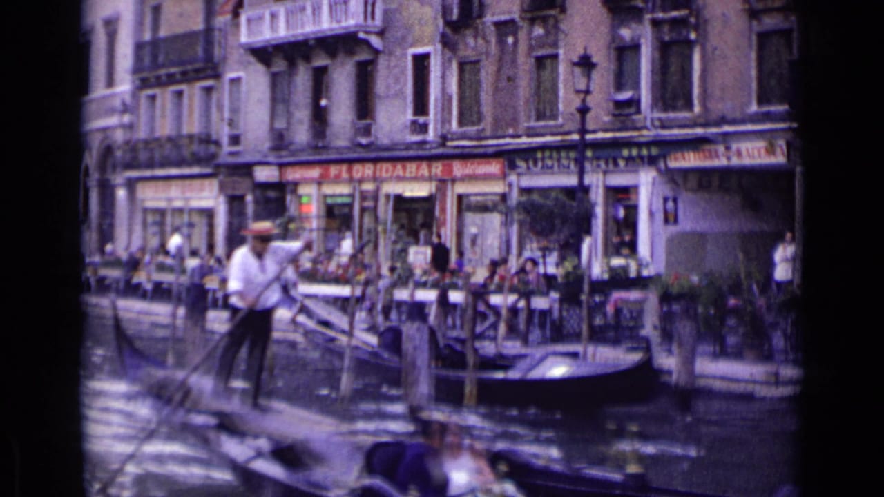 1962 Venice canal view from a gondola, with a gondolier in a white shirt passing cafe tables and Floridabar Ristorante signage.