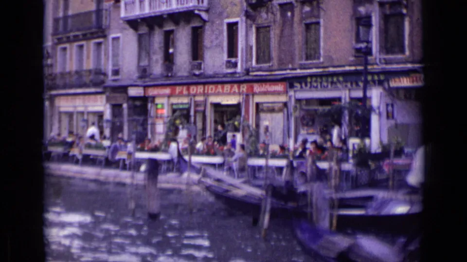 1962 Venice canal scene showing Floridabar Ristorante frontage, seated patrons, mooring posts, and part of a gondola in the foreground.