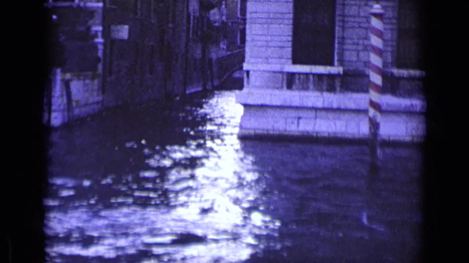 Venice canal scene from 1962 with reflective water, stone architecture, and striped mooring posts along the edge.