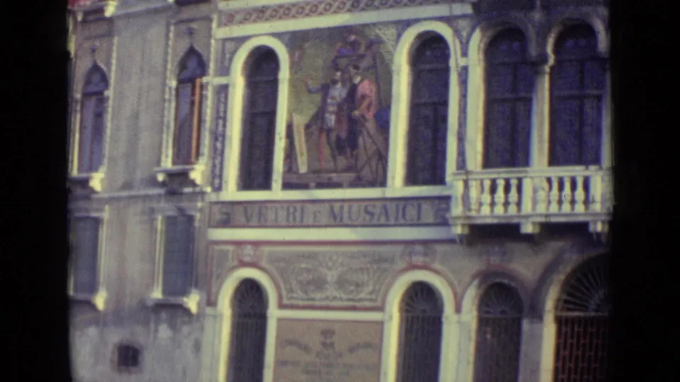 1962 Venice 8mm frame showing Vetri e Musaici lettering below mural figures, with tall arched windows and a small projecting balcony.