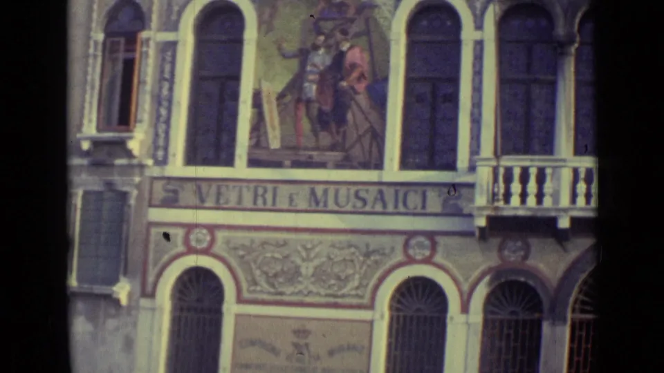 1962 Venice 8mm frame showing a decorated canal-side facade with arched windows, a balcony, and VETRI E MUSAICI lettering.
