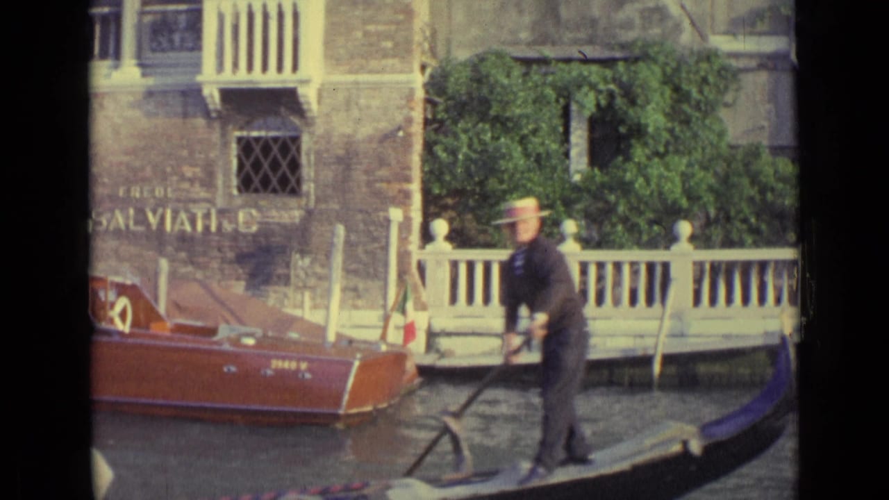 Gondolier steering a gondola beside a canal wall with Salviati signage and a red motorboat.