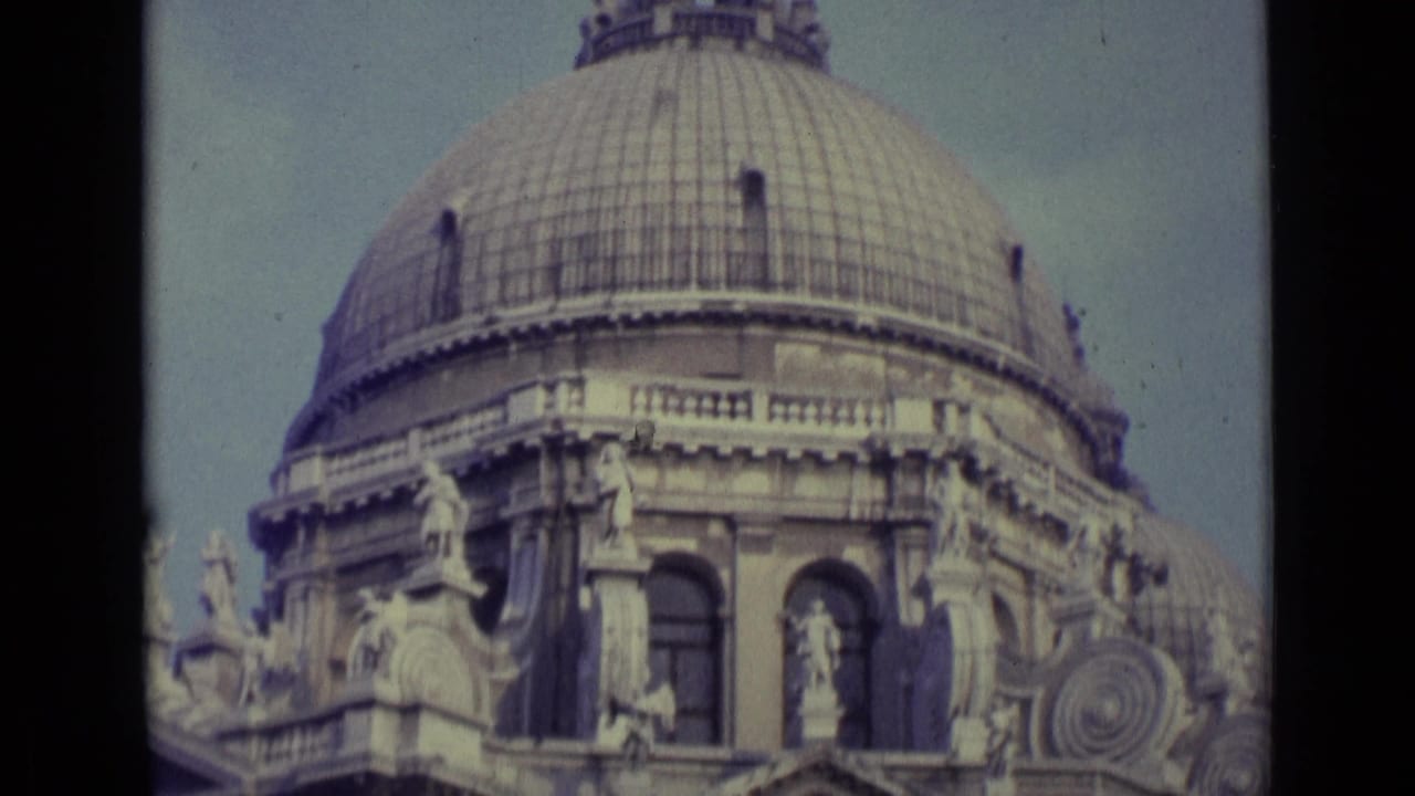 1962 Venice 8mm frame showing the upper dome, sculptural details, and arched windows of an ornate historic stone landmark.
