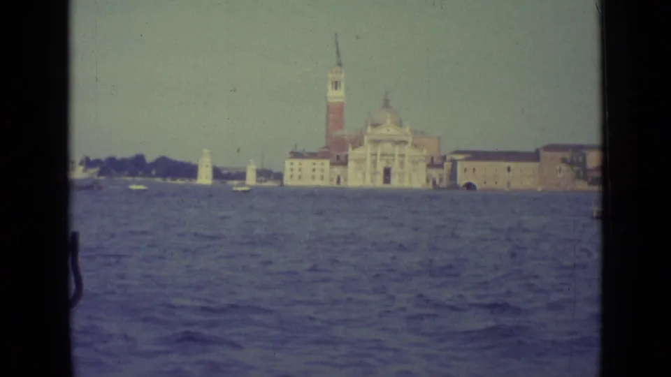 1962 Venice lagoon footage showing San Giorgio Maggiore and its bell tower across rippling water, framed by a boat window.