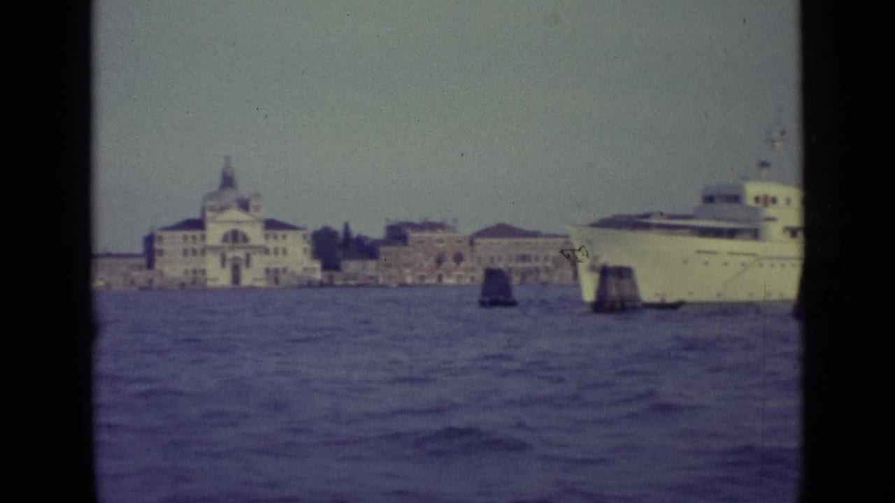 White ship passing across choppy water with historic Venetian waterfront buildings behind it.