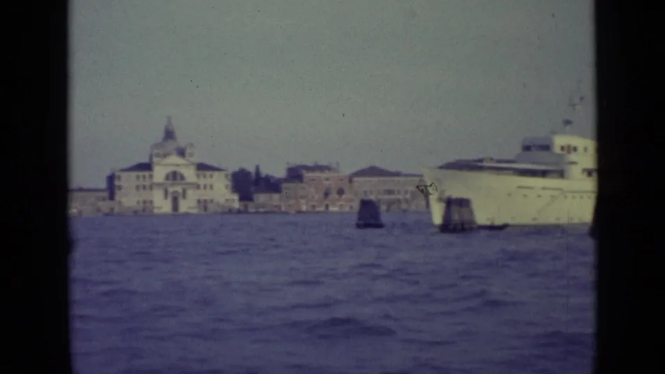 1962 Venice 8mm frame showing a large white ship crossing in front of waterfront buildings and a domed church-like structure.