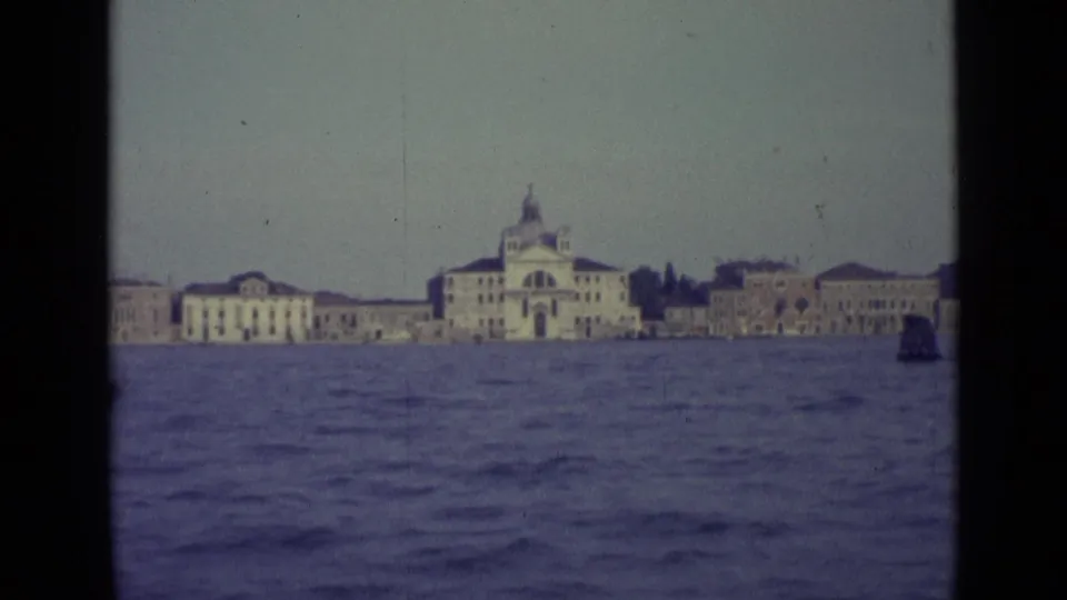 1962 Venice 8mm frame with a domed church-like waterfront building and pale historic facades across choppy water.