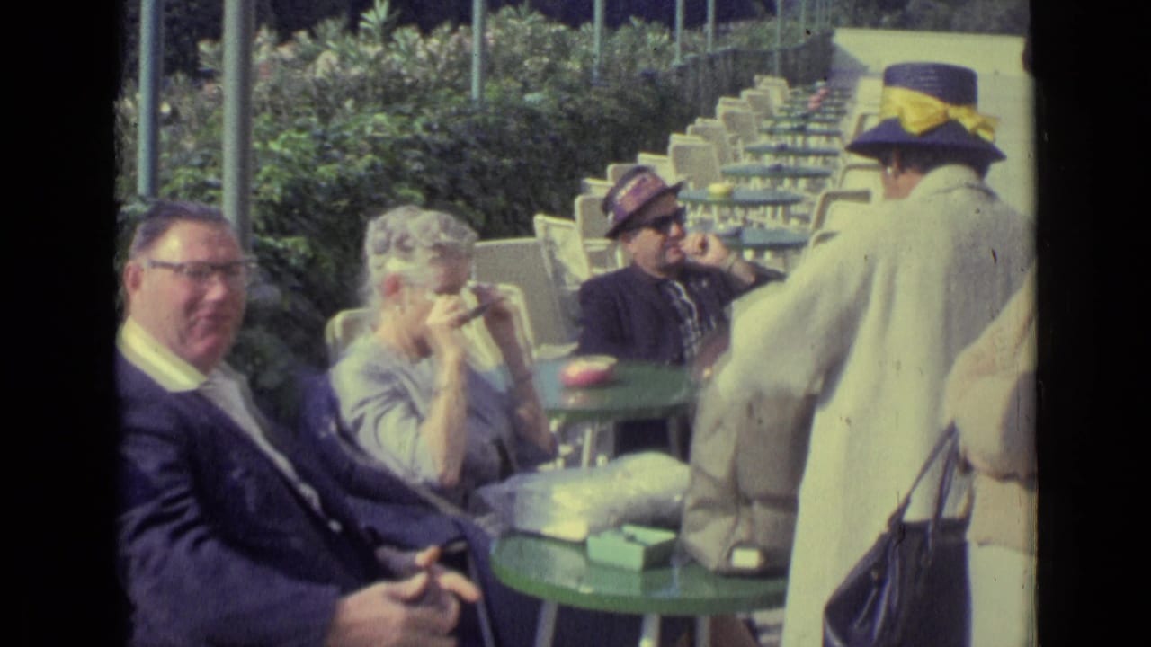 Seated café group with a man in glasses, a woman drinking, and another man in sunglasses nearby.