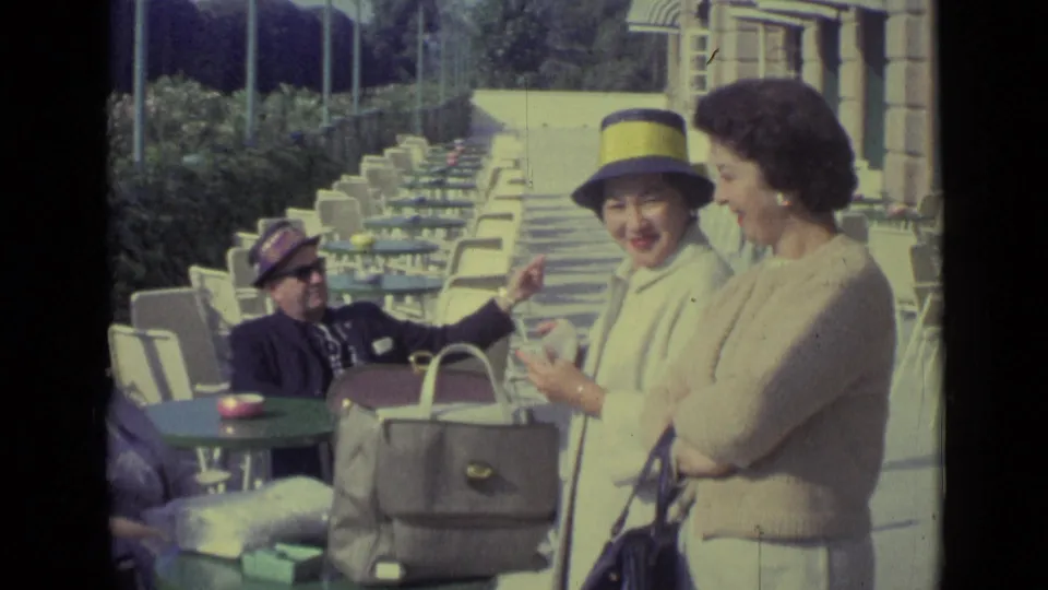 1962 Venice outdoor café frame showing two women in conversation, including one in a blue hat with a yellow band.