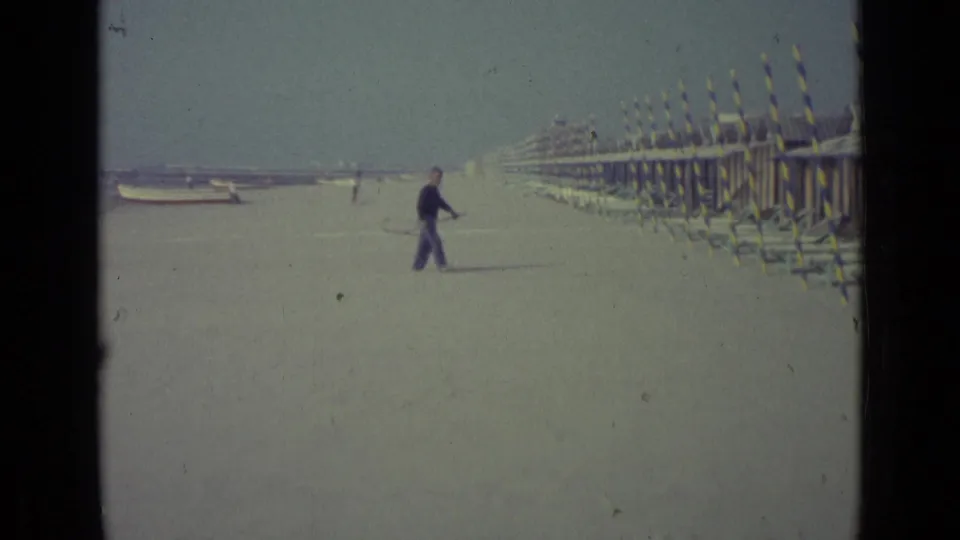 Final frame shows the man with the long-handled net near the cabanas, with boats and distant beachgoers in the background.