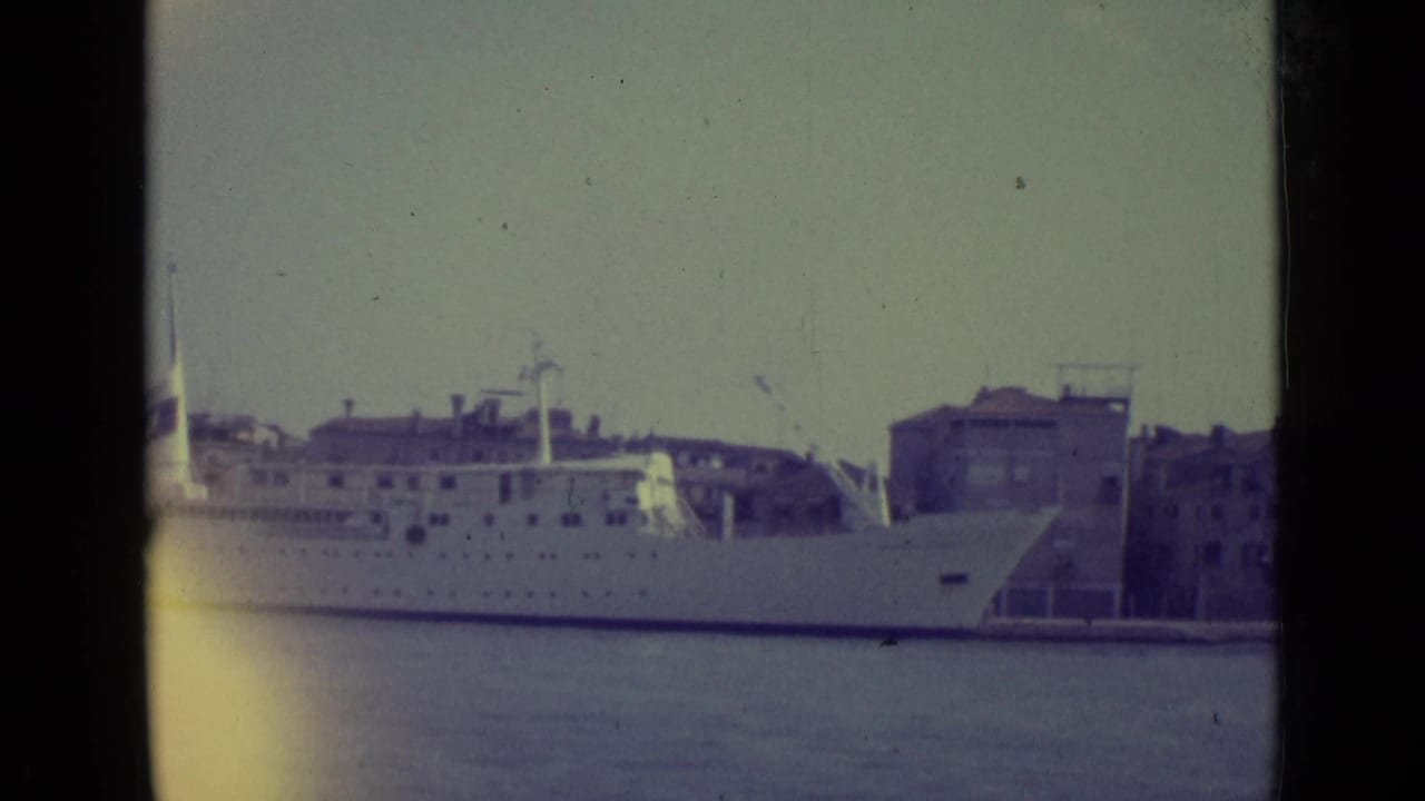 White passenger ship docked across Venetian harbor water with waterfront buildings behind it.