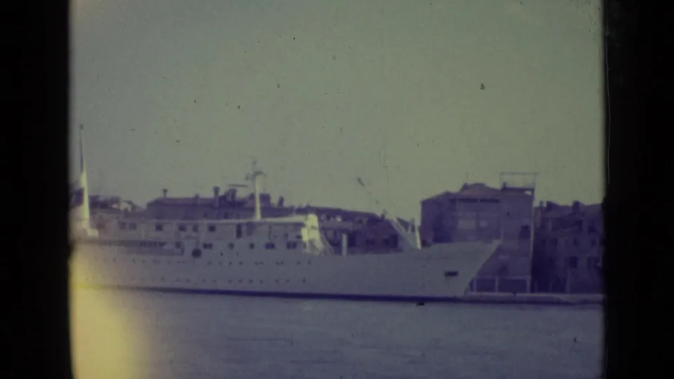 1962 Venice harbor view of a large white passenger ship seen from a distance on faded 8mm film.