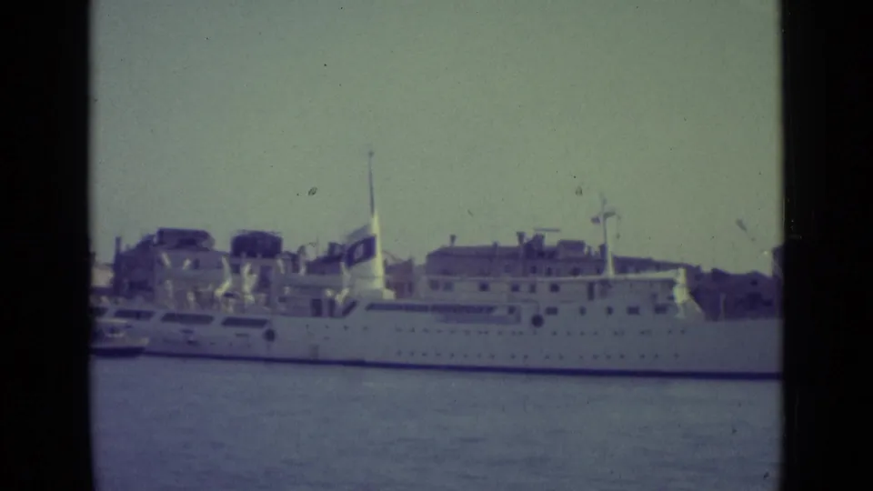 1962 Venice harbor shot with the white passenger ship centered, waterfront buildings in back, and aged 8mm film texture.