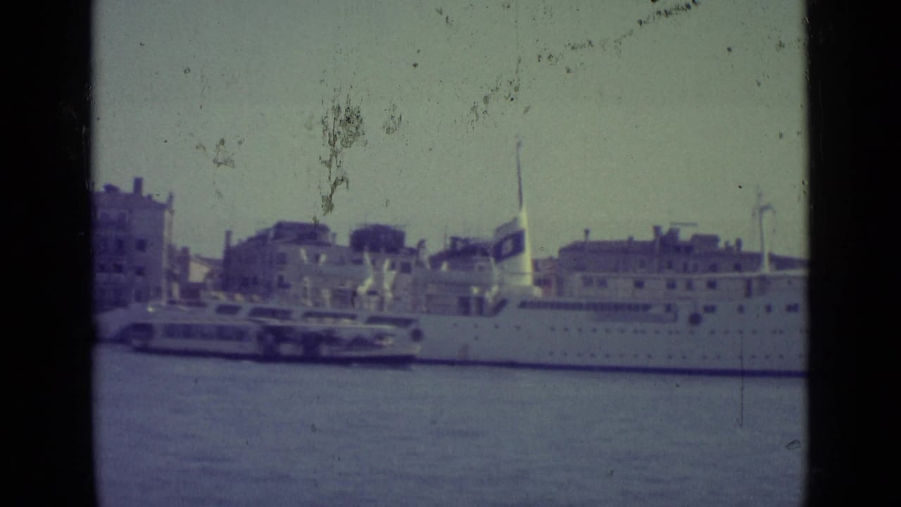 Docked white ship and small ferry beside waterfront buildings across the canal.