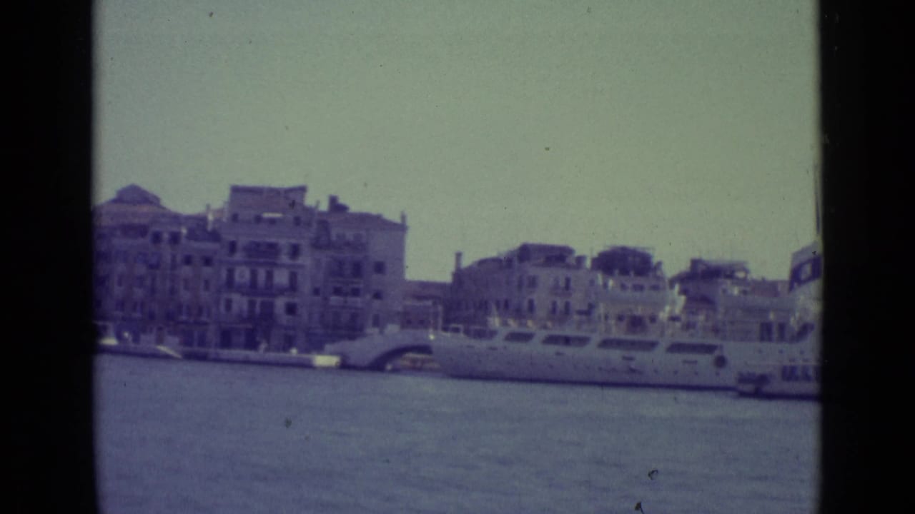 Large boat near waterfront buildings with canal water in the foreground.