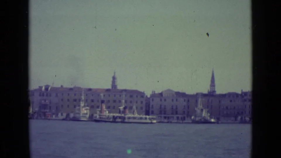 End frame of 1962 Venice 8mm footage showing canal water, moored boats, pale buildings, and distant spires.