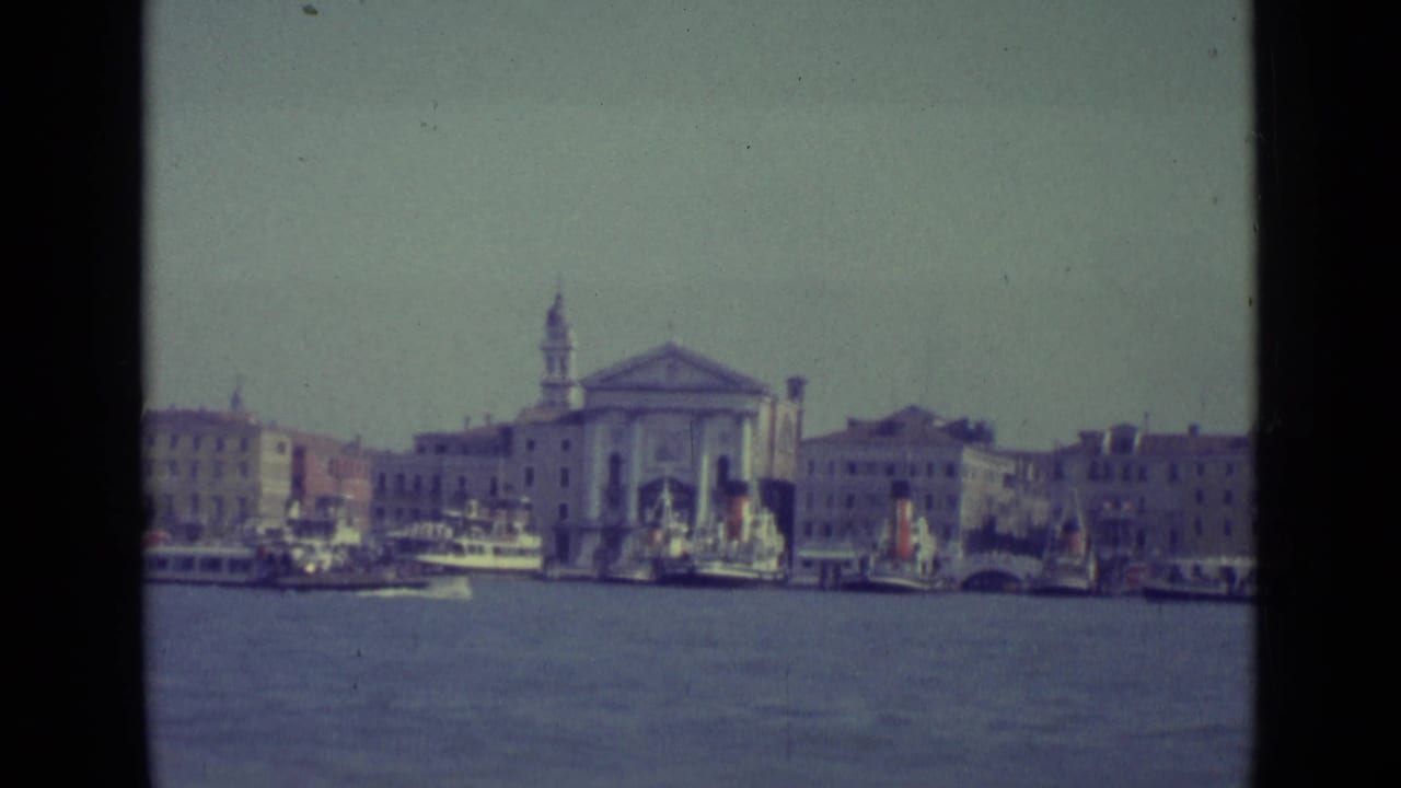 Waterfront buildings and boats with a church and bell tower across the water.