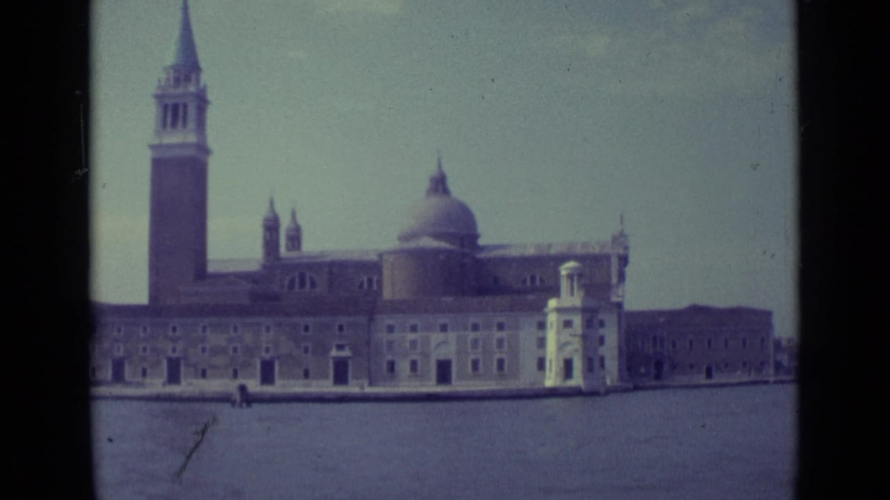 Venice waterfront building with bell tower and dome seen across lagoon water.