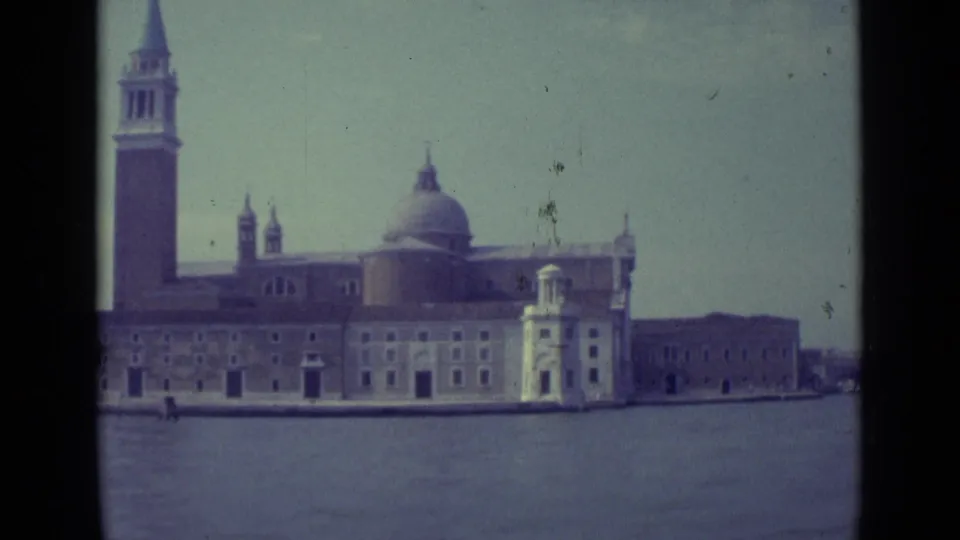 Venice lagoon view of the same historic waterfront building, with the bell tower at left and a small bright structure near the quay.