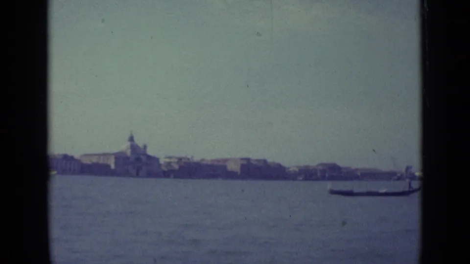1962 Venice waterfront seen from the lagoon, with a distant domed church and a gondola partly visible near the right side of the frame.