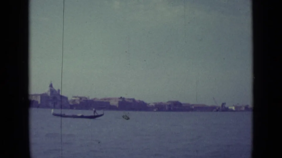A gondola glides across the Venice lagoon in 1962 home-movie footage, with distant domes and low buildings beyond.