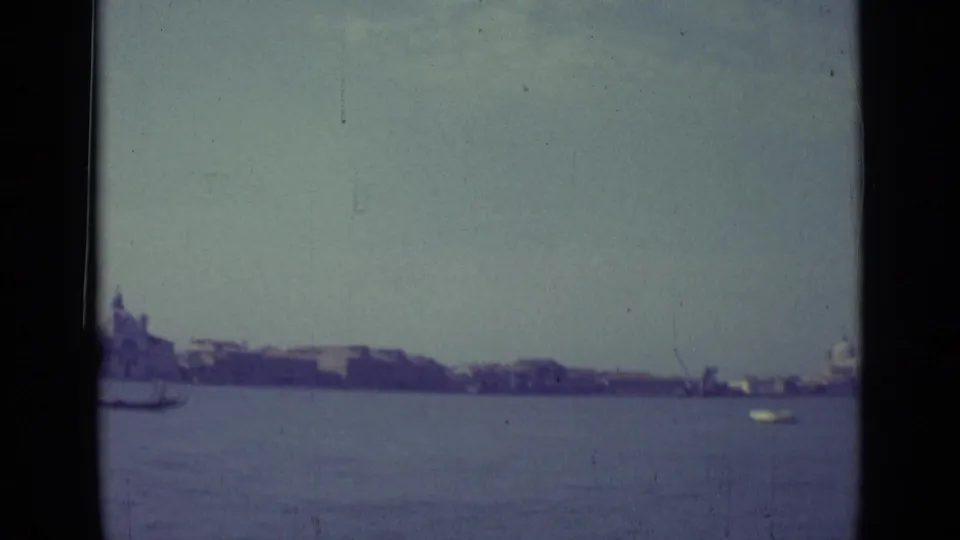 A wider 1962 Venice lagoon view shows the gondola partly leaving frame, distant waterfront buildings, and a small bright boat.
