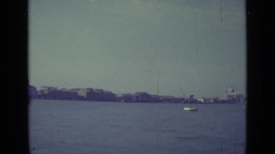 The final frame holds on Venice across the lagoon, with a small boat on the water and a domed building at the right edge.