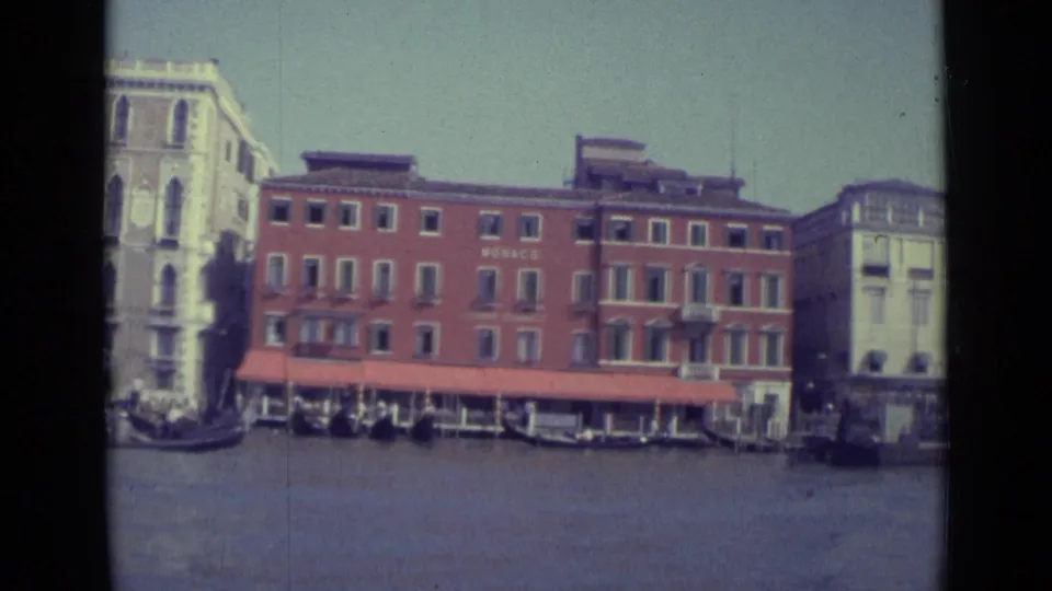 Later frame of the 1962 Venice canal pass, with the red MONACO building, awning, gondolas, and adjacent waterfront architecture.