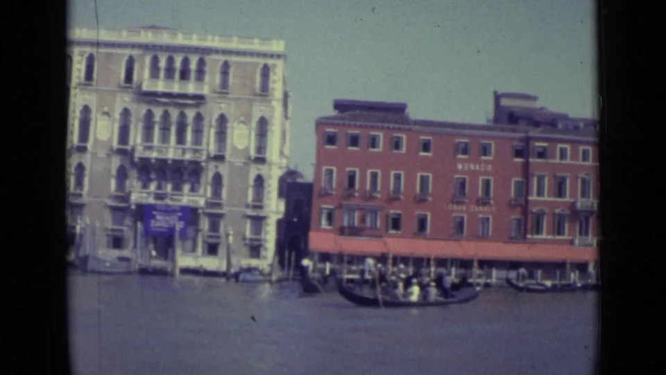 1962 Venice Grand Canal view centered on a pale palazzo and red MONACO building, with a gondola and small figures near the waterline.