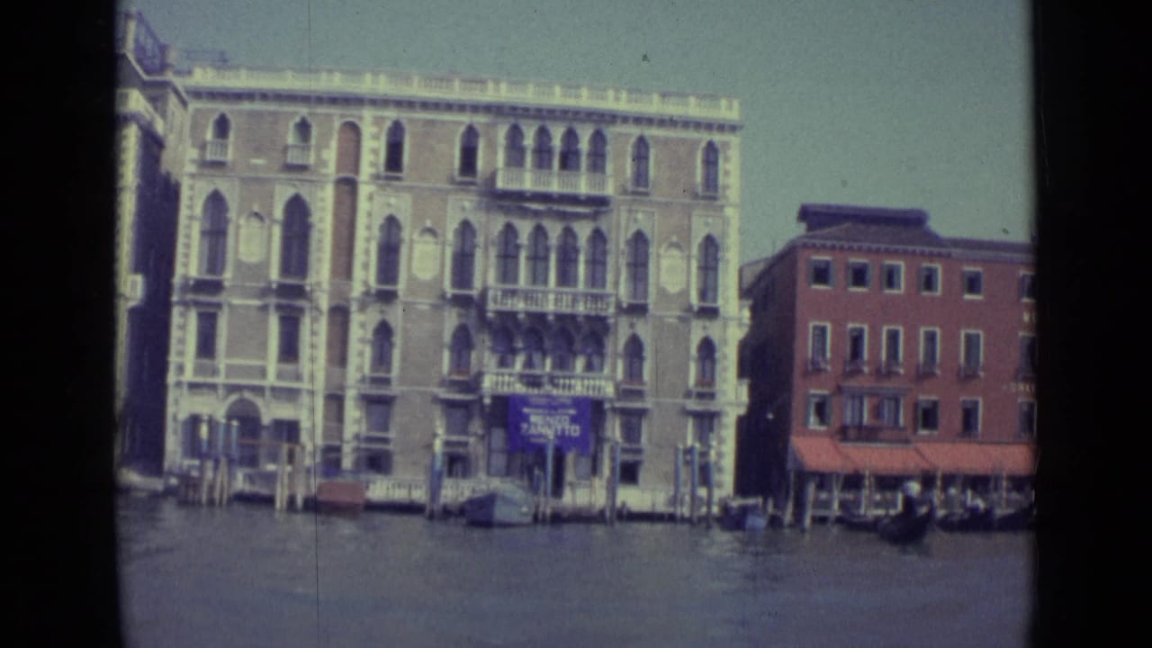 Similar canal view with ornate waterfront buildings, mooring poles, and a red MONACO facade.