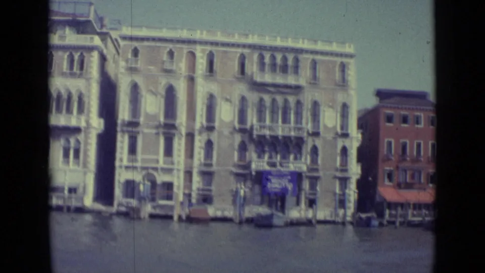 1962 Venice canal scene with a closer crop on ornate arched facades, balconies, canal water, mooring poles, and visible signs.