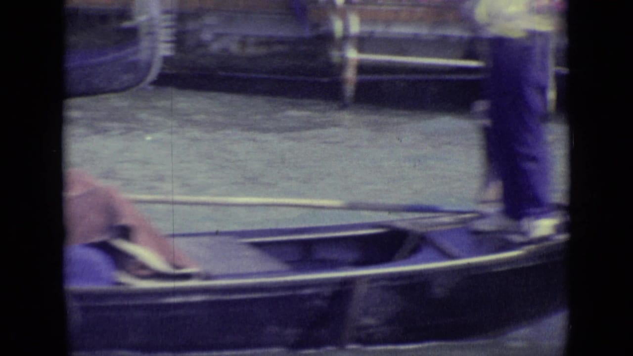 Gondola beside a canal with a standing gondolier partly visible.