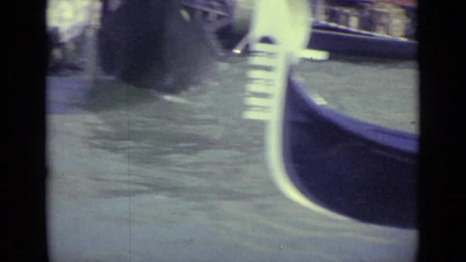 Close 8mm view of canal water and the curved prow of a gondola during a Venice travel shot.