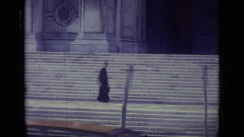1962 Venice 8mm frame showing a robed adult man on broad stone steps near a large architectural facade.