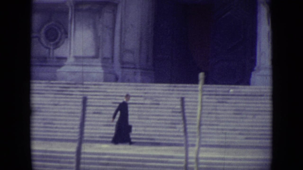 Priest in a dark cassock walking along wide stone steps before ornate columns.