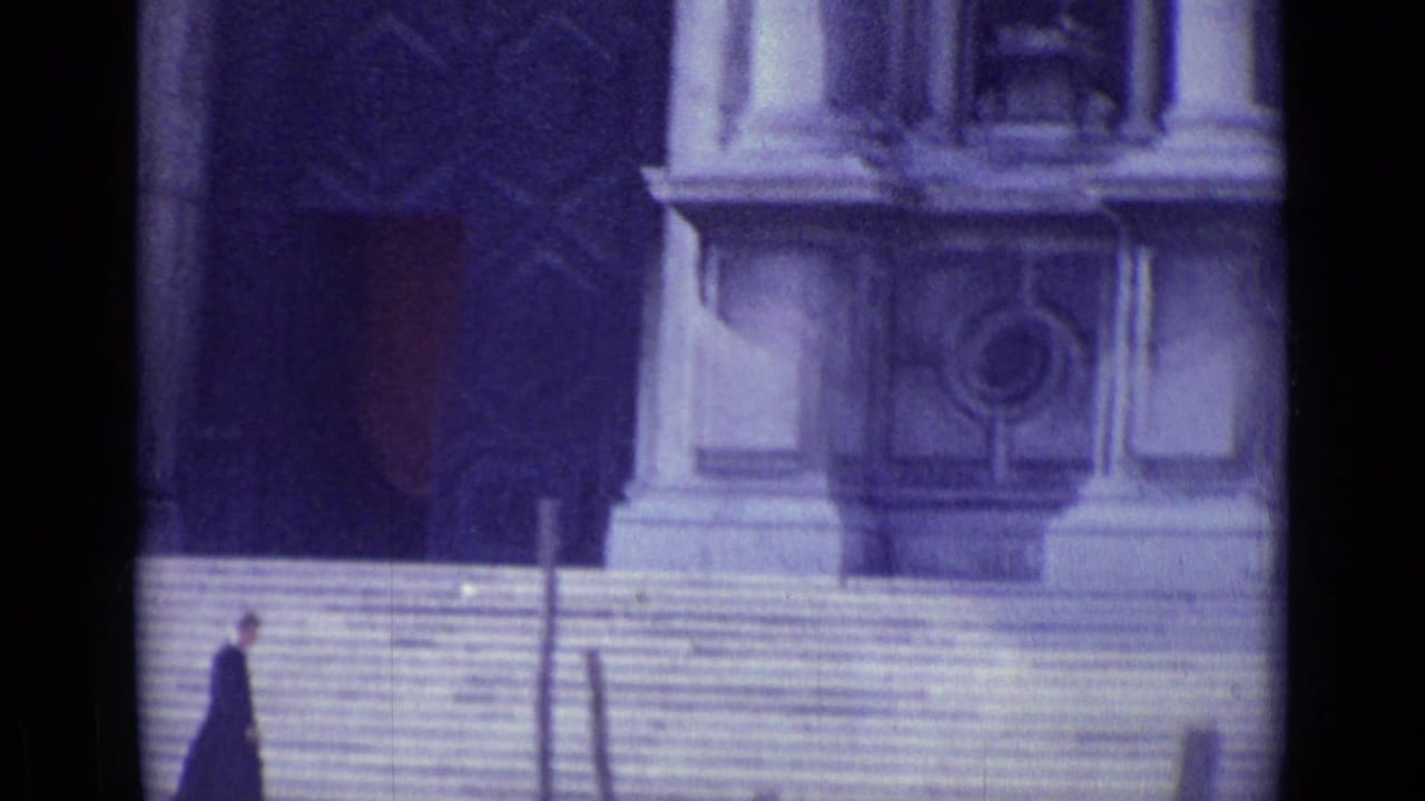 Priest walking along steps with a large columned facade behind him.