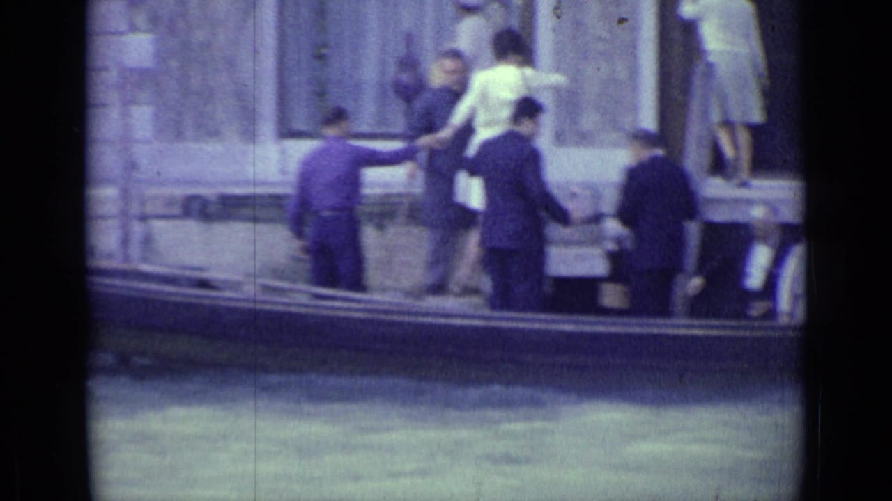 1962 Venice canal scene with tourists boarding or leaving a gondola beside a stone building.