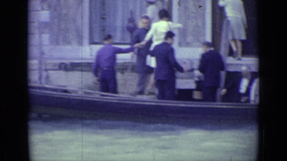 1962 Venice canal scene with tourists boarding or leaving a gondola beside a stone building.