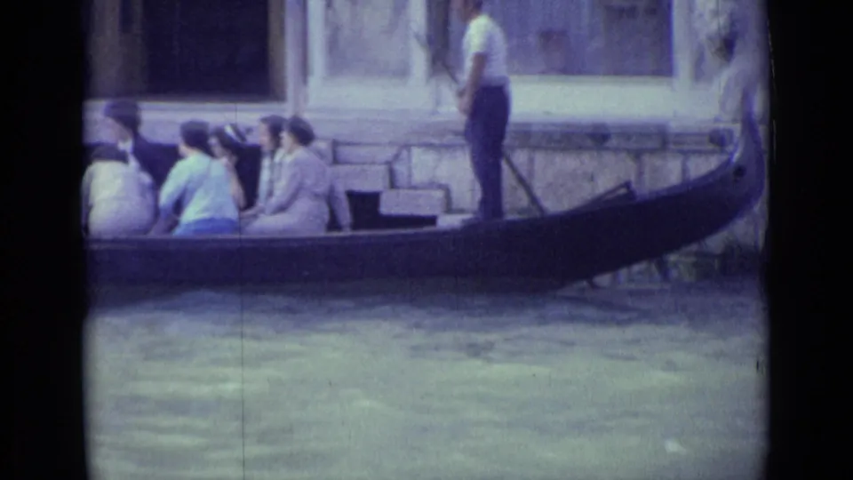 1962 Venice gondola ride with seated passengers and a standing gondolier beside canal-side steps.