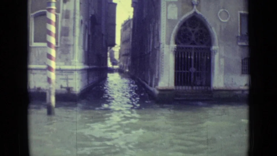 Venice canal view with water-level masonry, an arched gated opening, and a striped mooring pole.