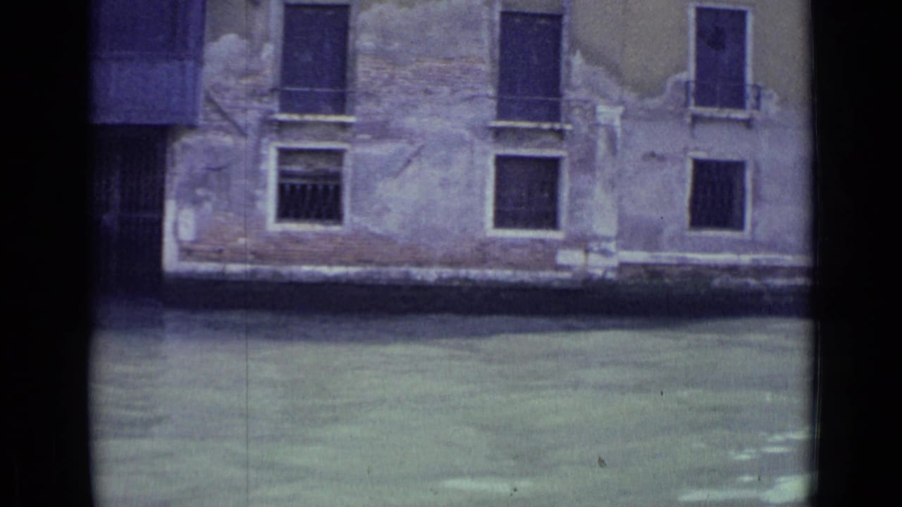 Canal water in front of a weathered building facade with shuttered windows.